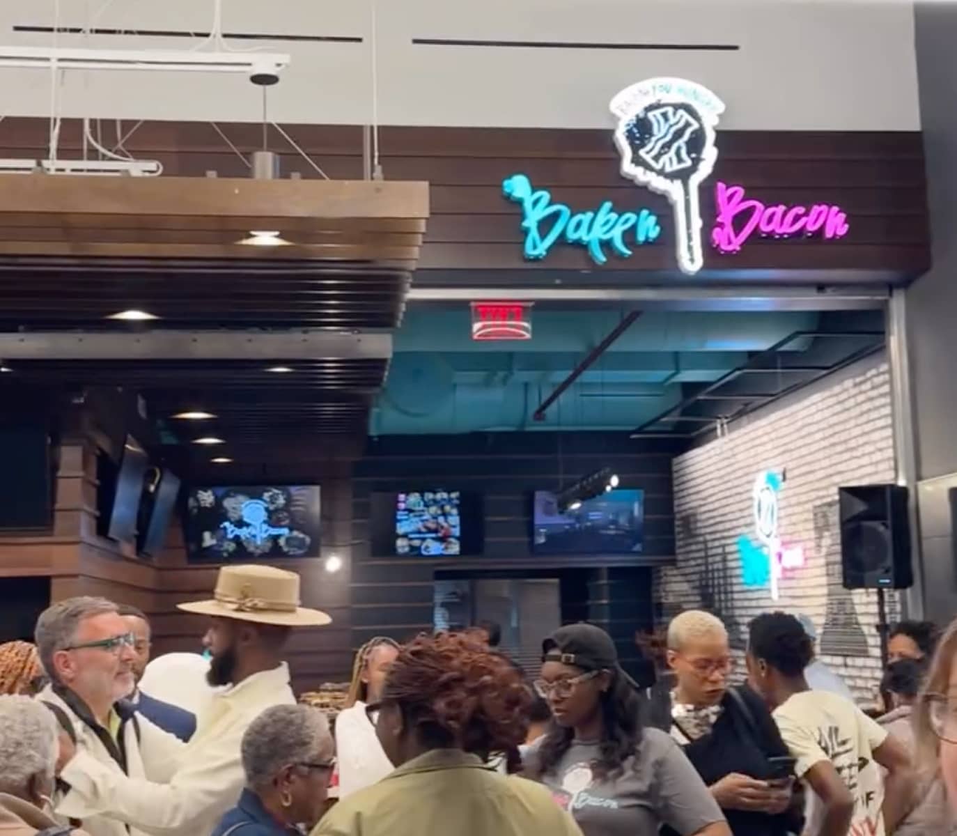 A bustling crowd gathers inside a modern eatery with a neon sign reading 