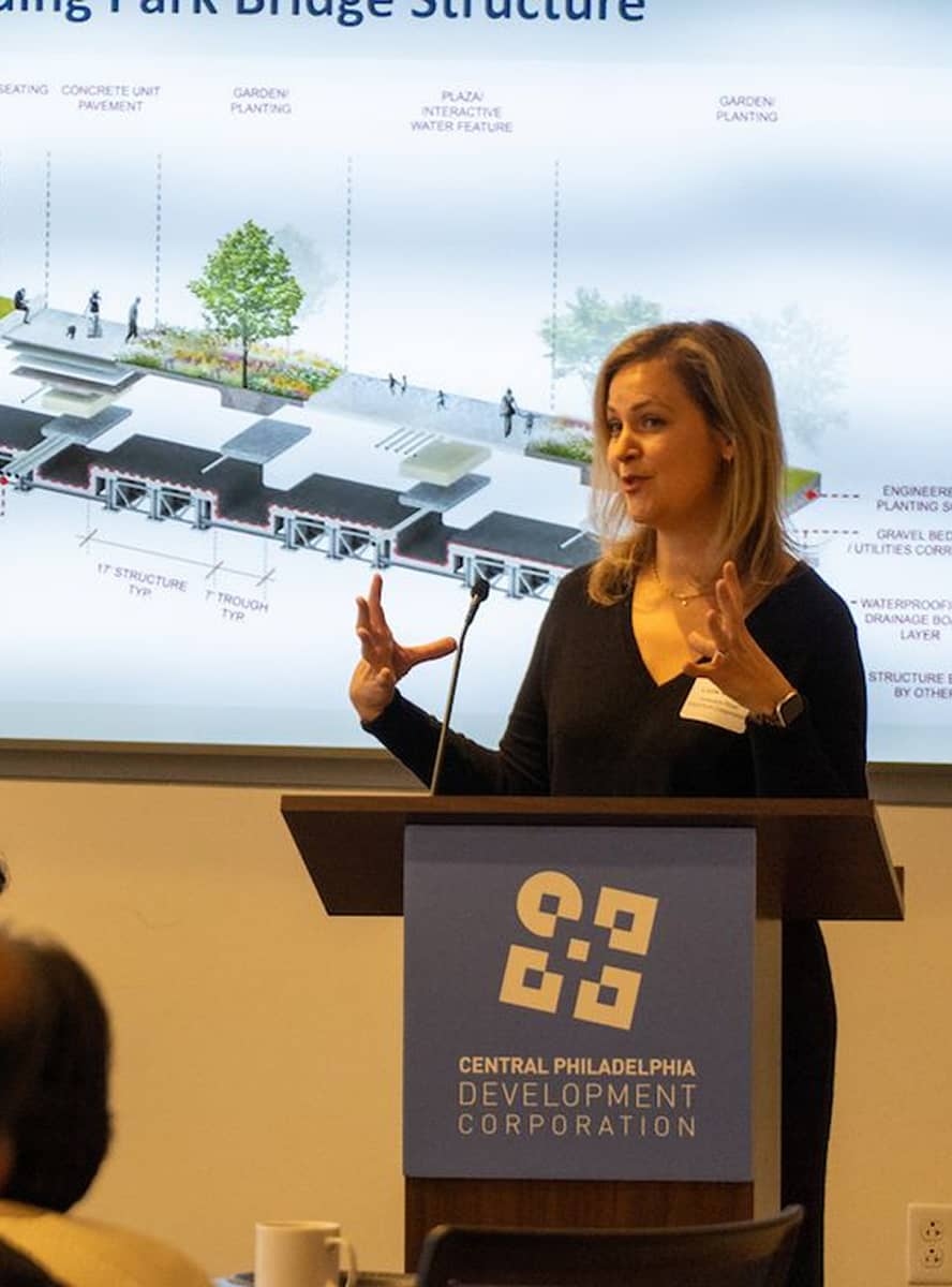 A woman gestures while speaking at a podium with a 