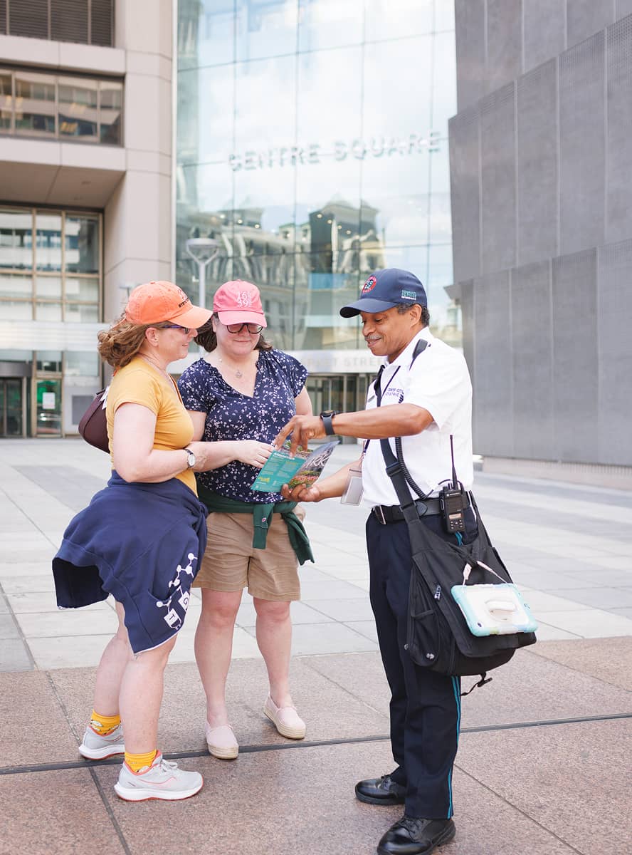 Two women in casual attire consult a map with a helpful guide outside a modern building labeled 