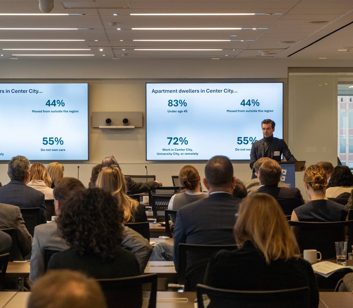 Audience listening to a speaker at a conference room. Two screens display statistics about apartment dwellers in Center City.